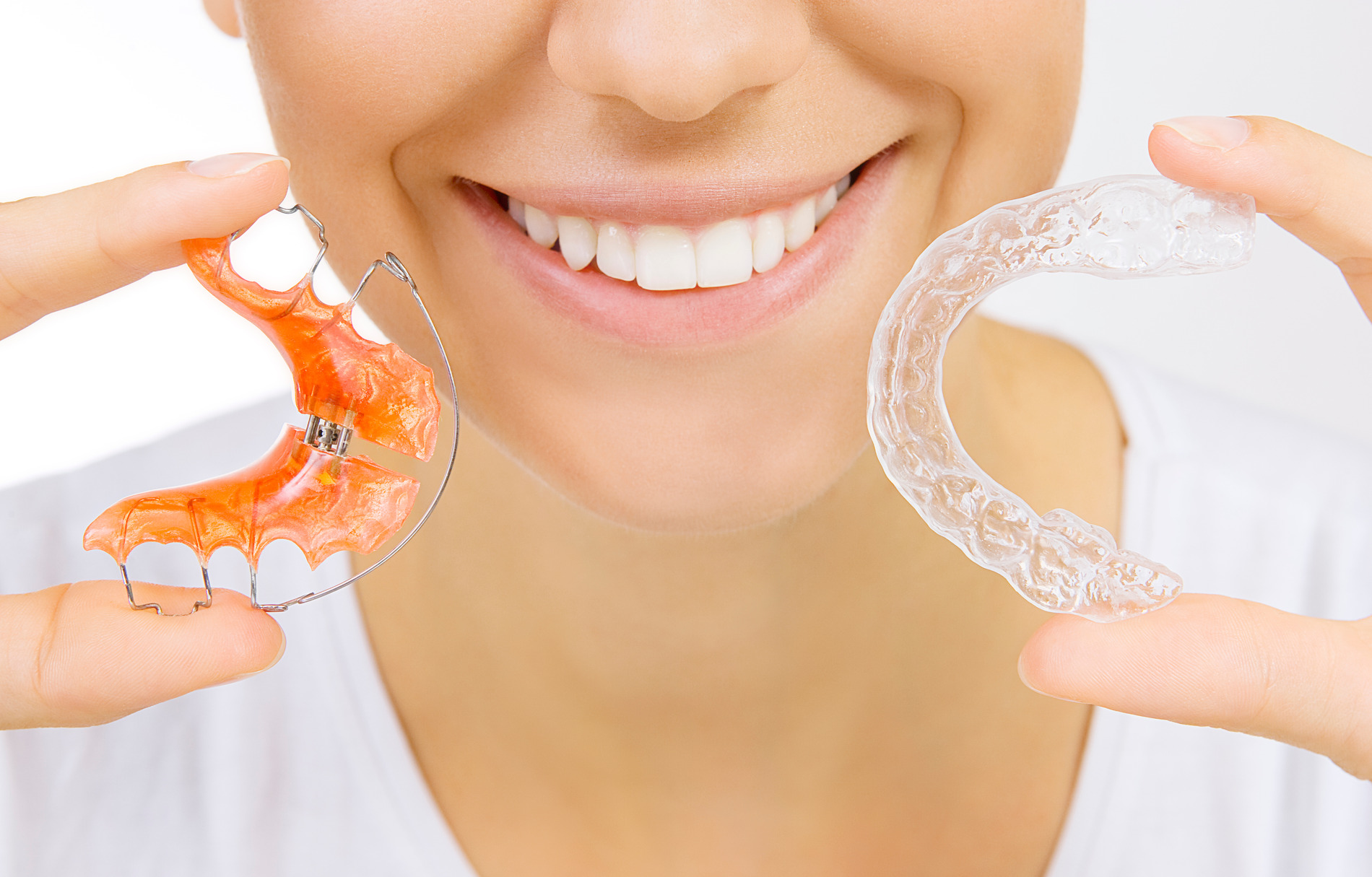 AdobeStock_56159139 v2 Womaning smiling and showing the two options for retainers, a metal retainer and clear retainer